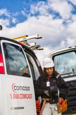 Female Comcast service technician working with handheld device outside of her work van.